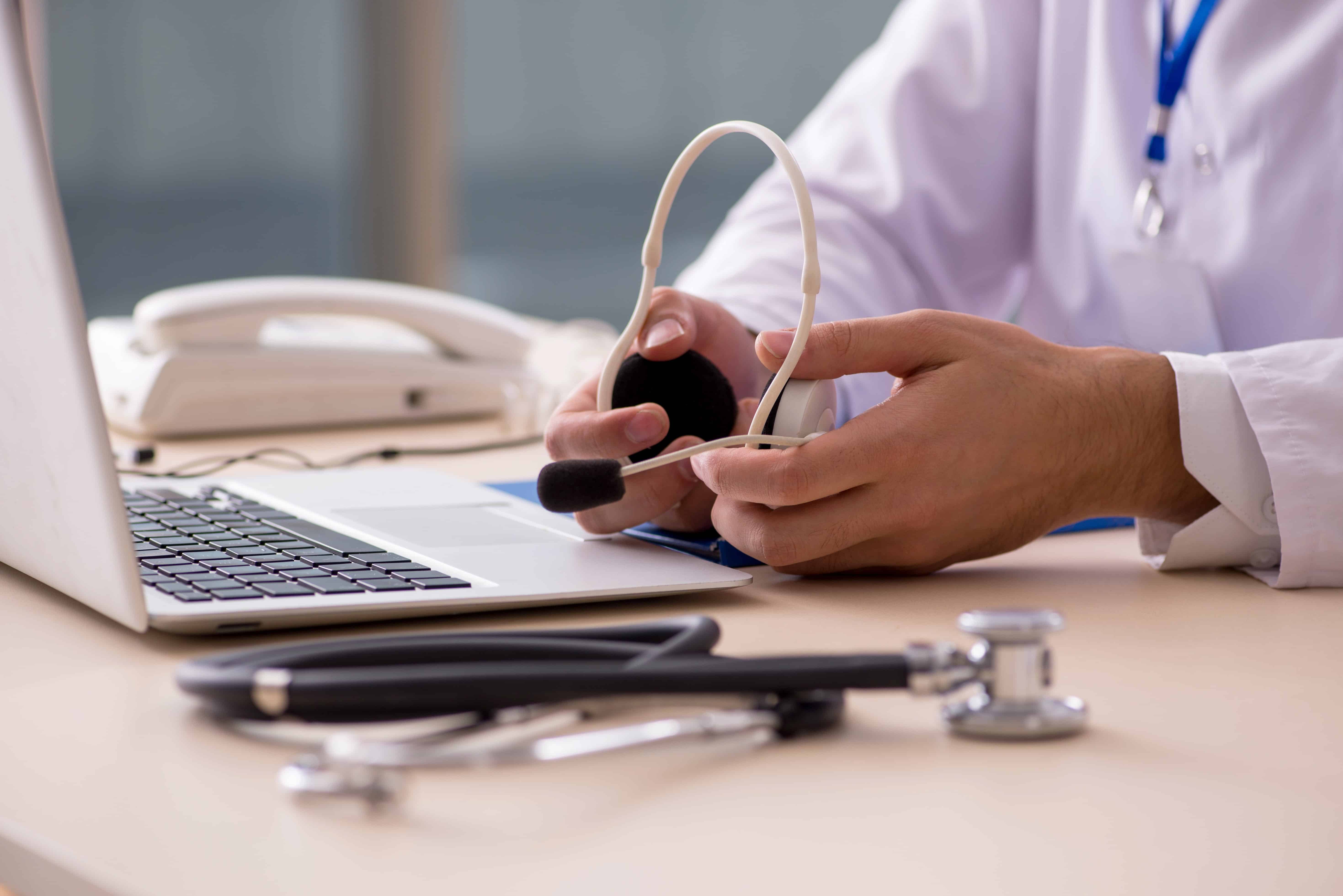 Close up of a medical professional with a headset, stethoscope, and laptop