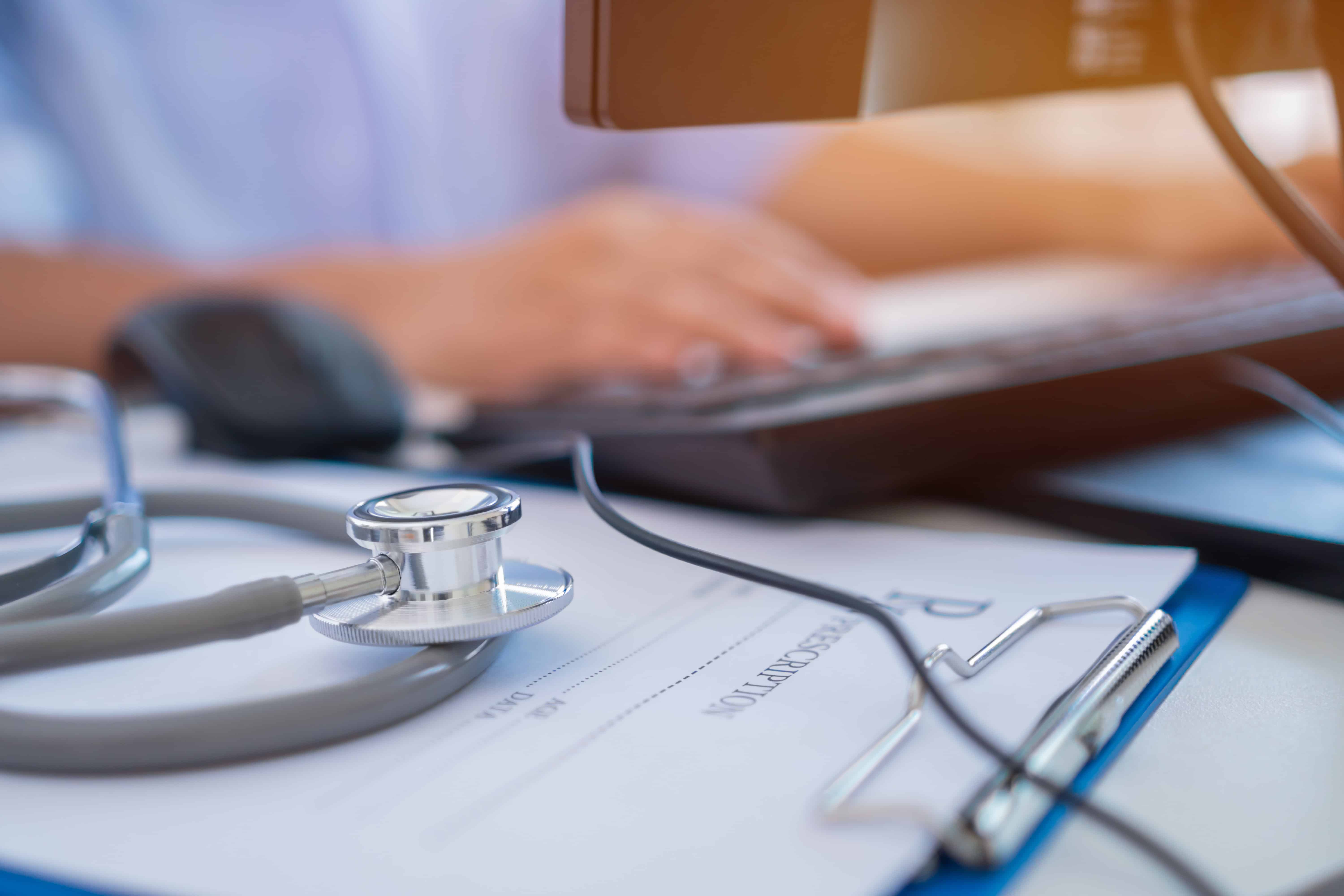 Medical professional with a stethoscope typing on a keyboard