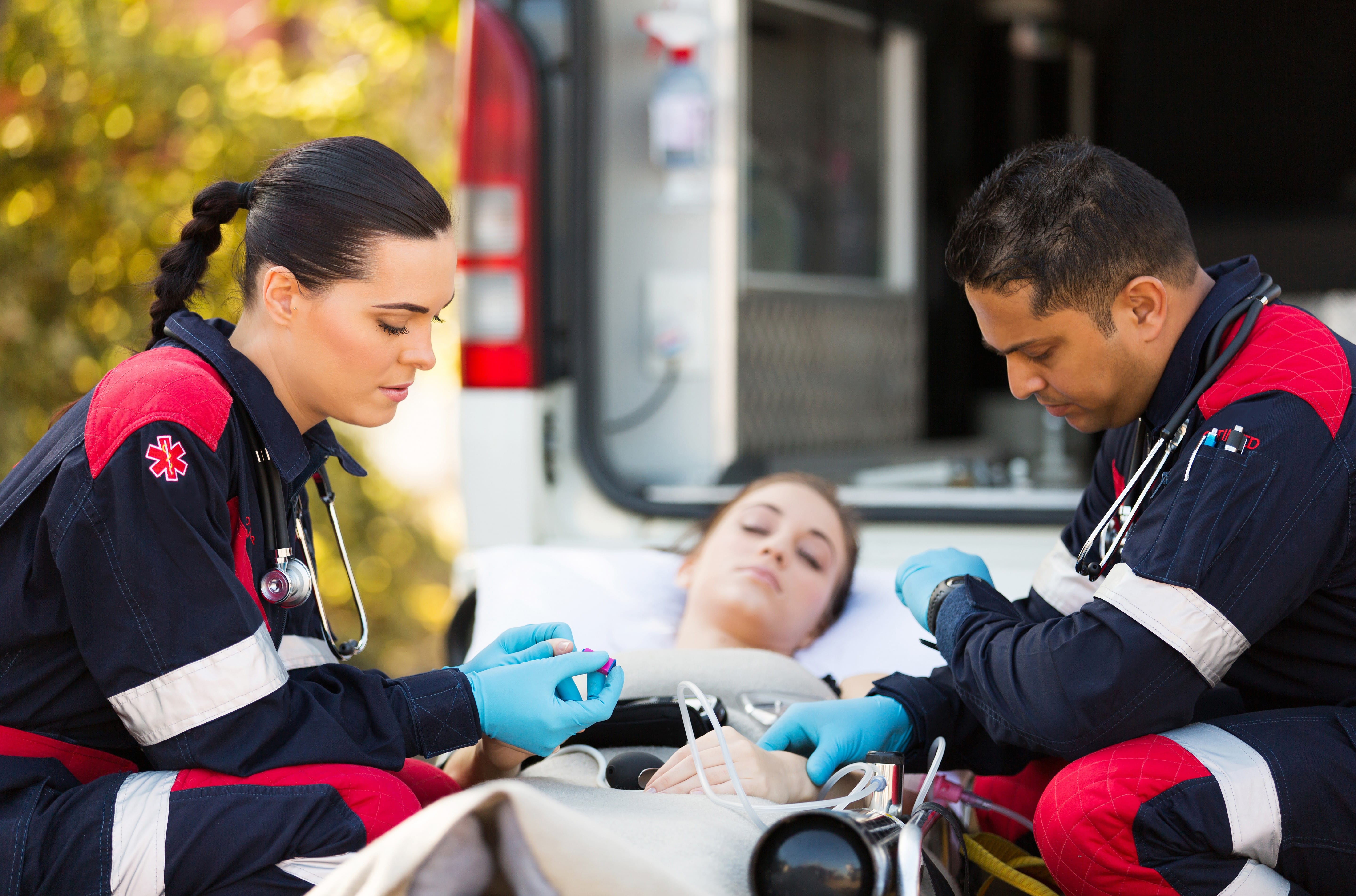 EMS professionals with stethoscopes assisting a woman on a stretcher