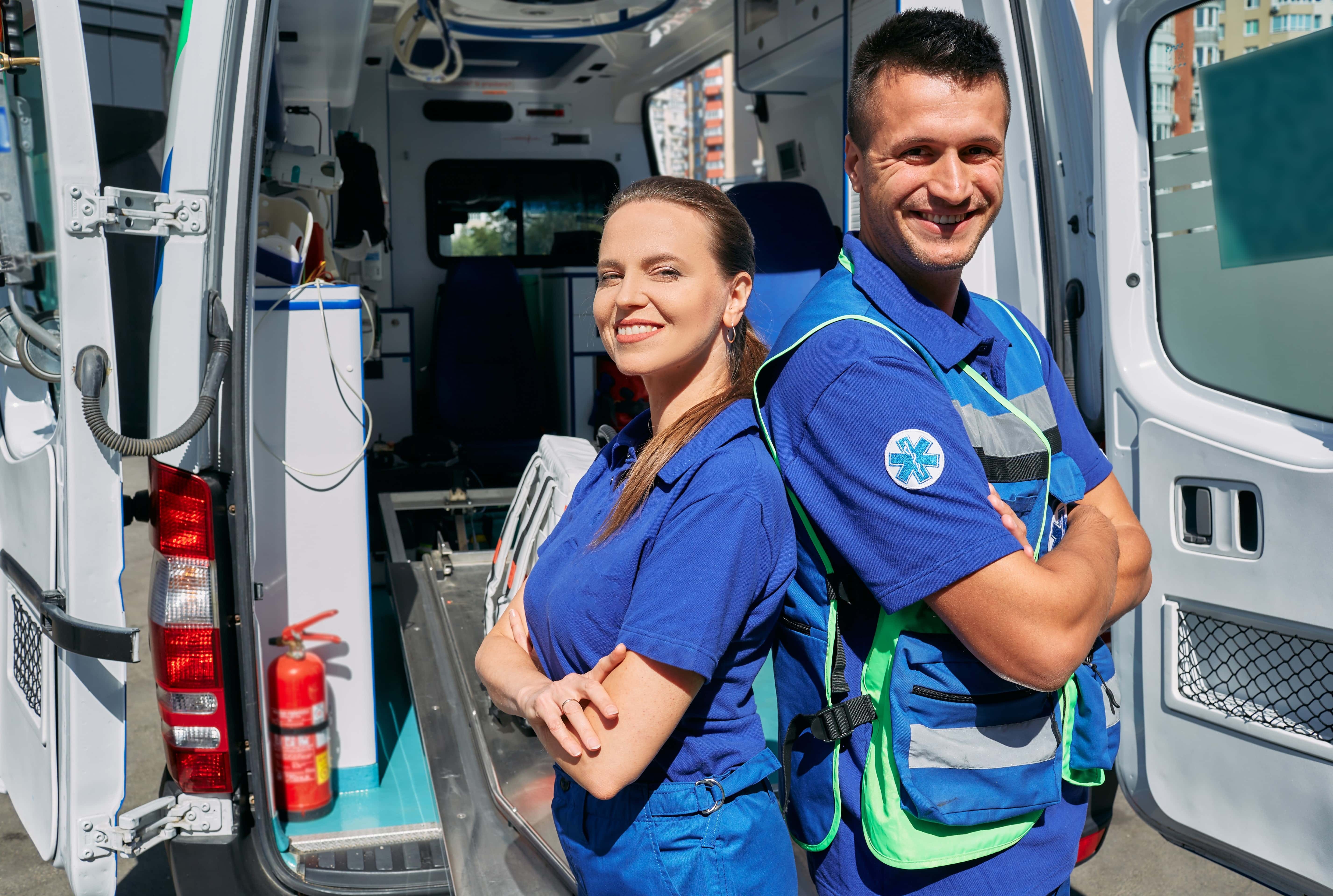 Two smiling EMS professionals in front of an ambulance
