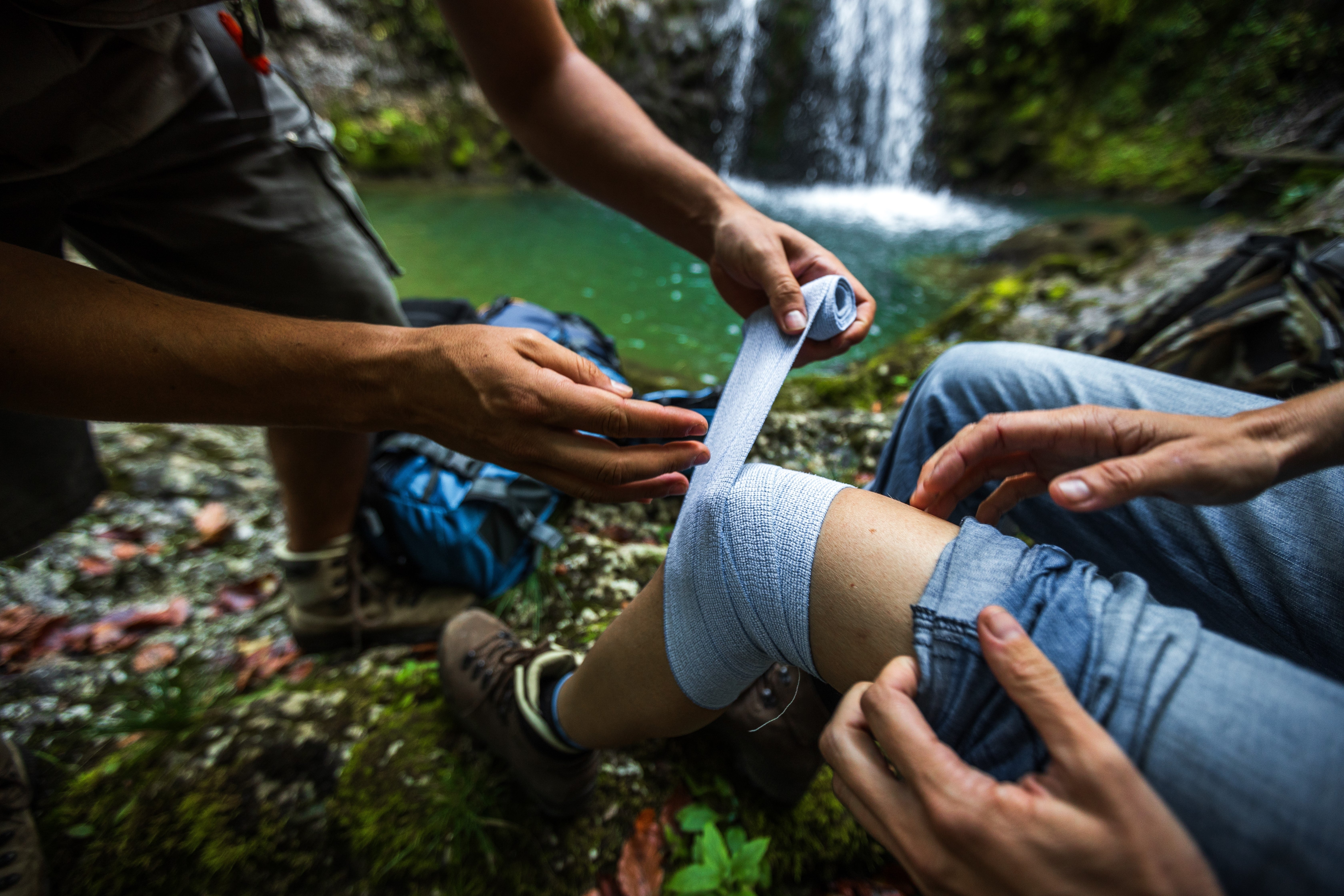 Man wrapping a person's knee with gauze beside a waterfall