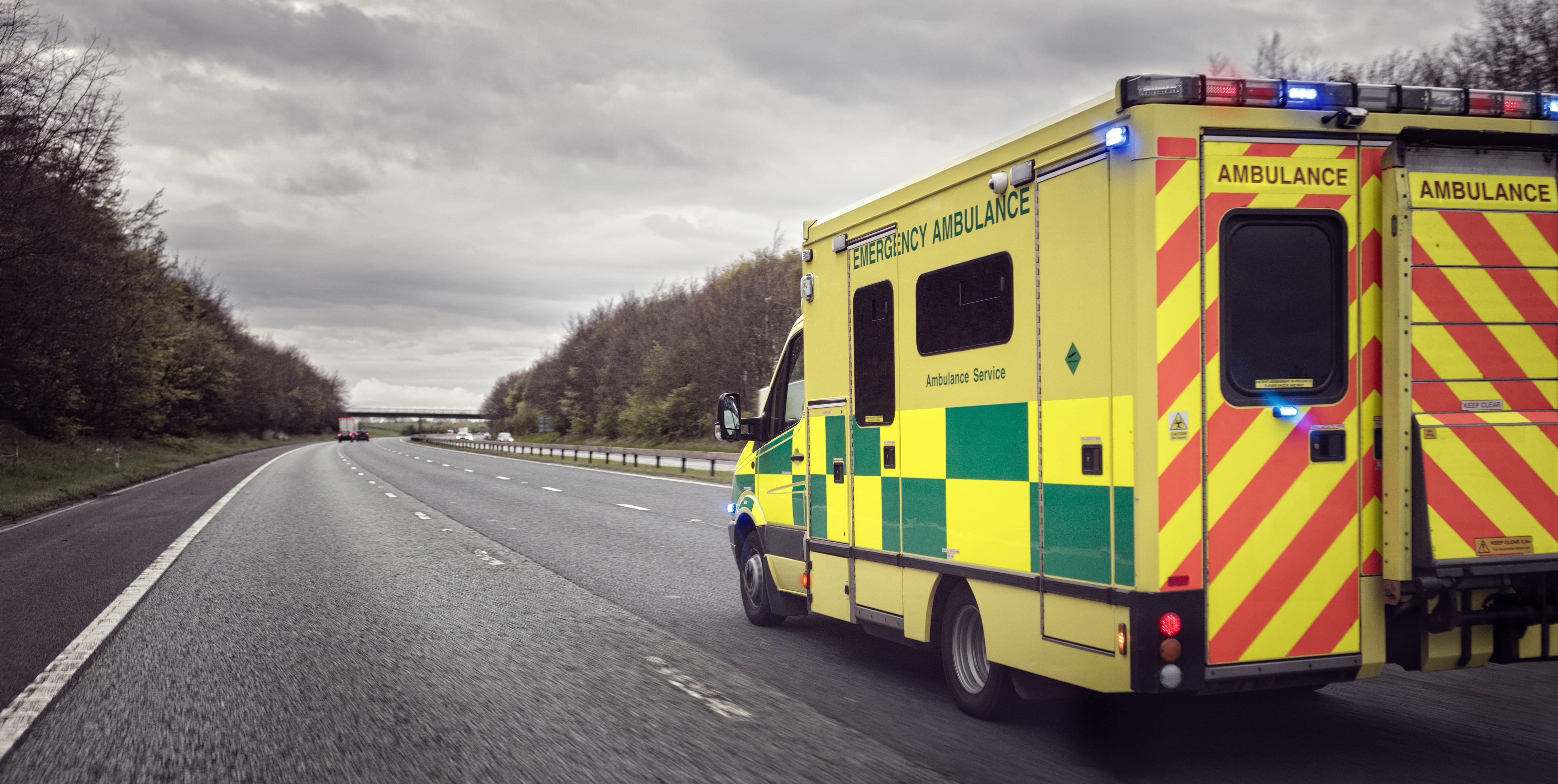 Ambulance driving on a freeway under an overcast sky