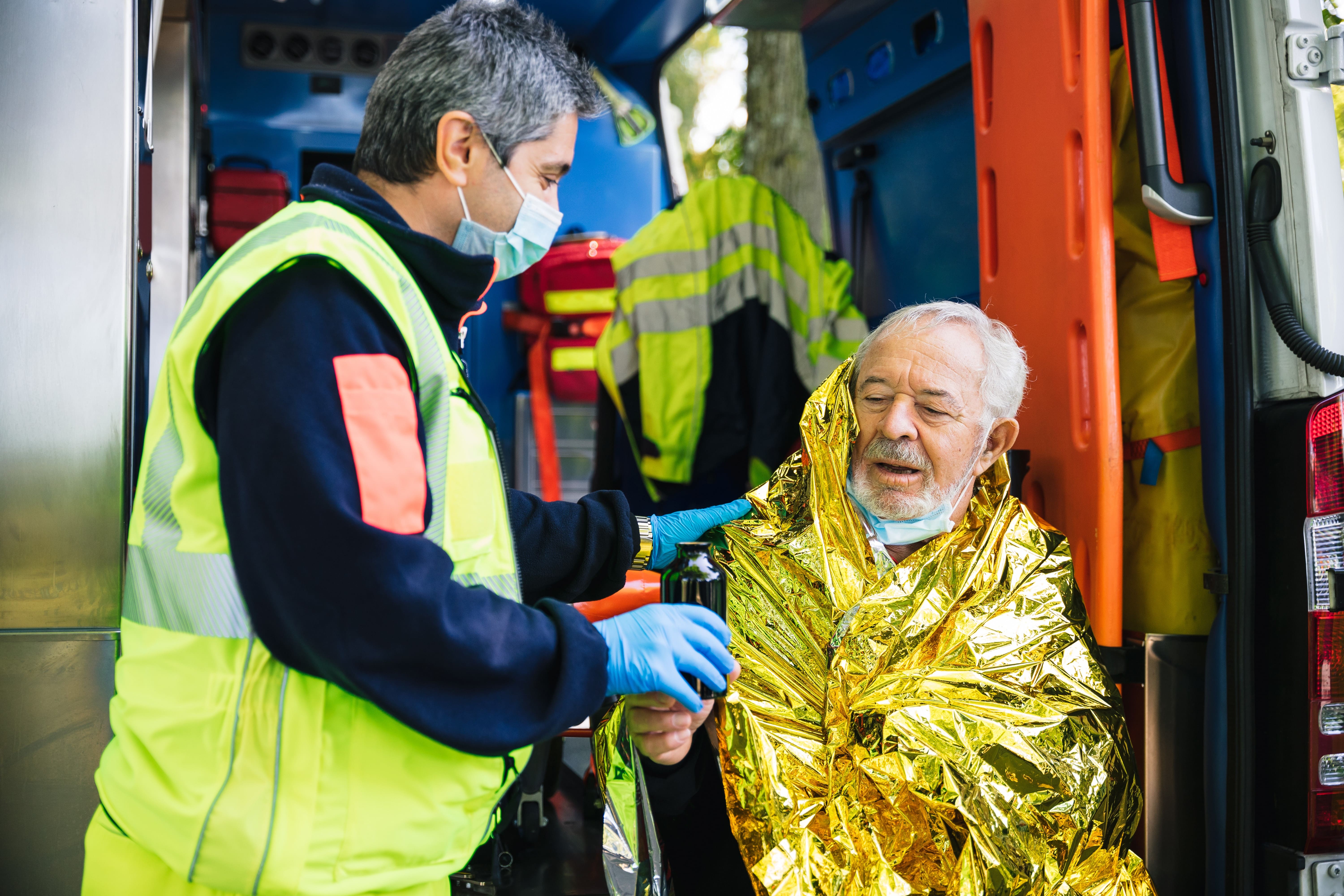 EMS professional placing an emergency blanket on an elderly man