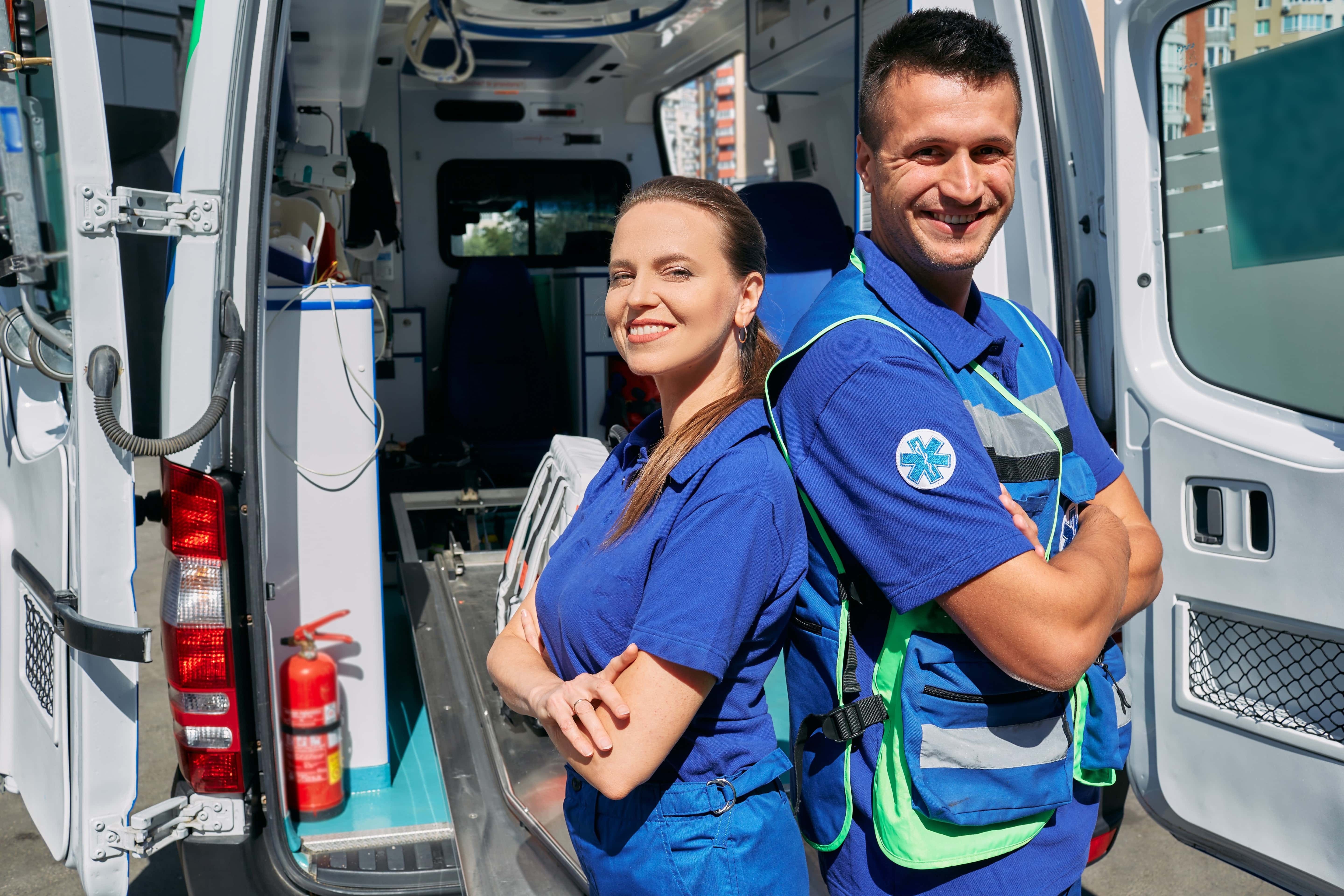 Two EMS professionals smiling in front of an ambulance