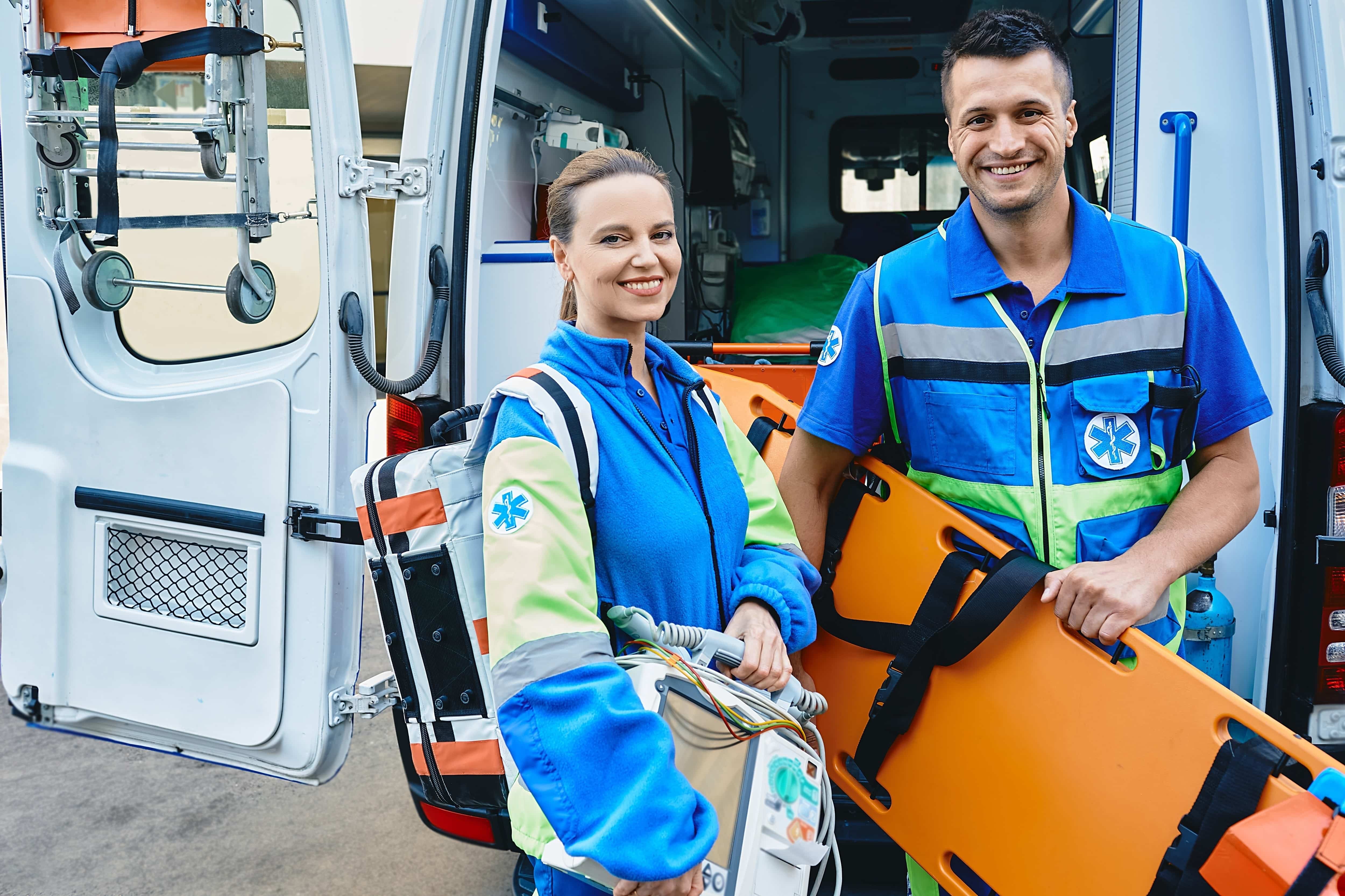 Two smiling EMS professionals in front of an ambulance