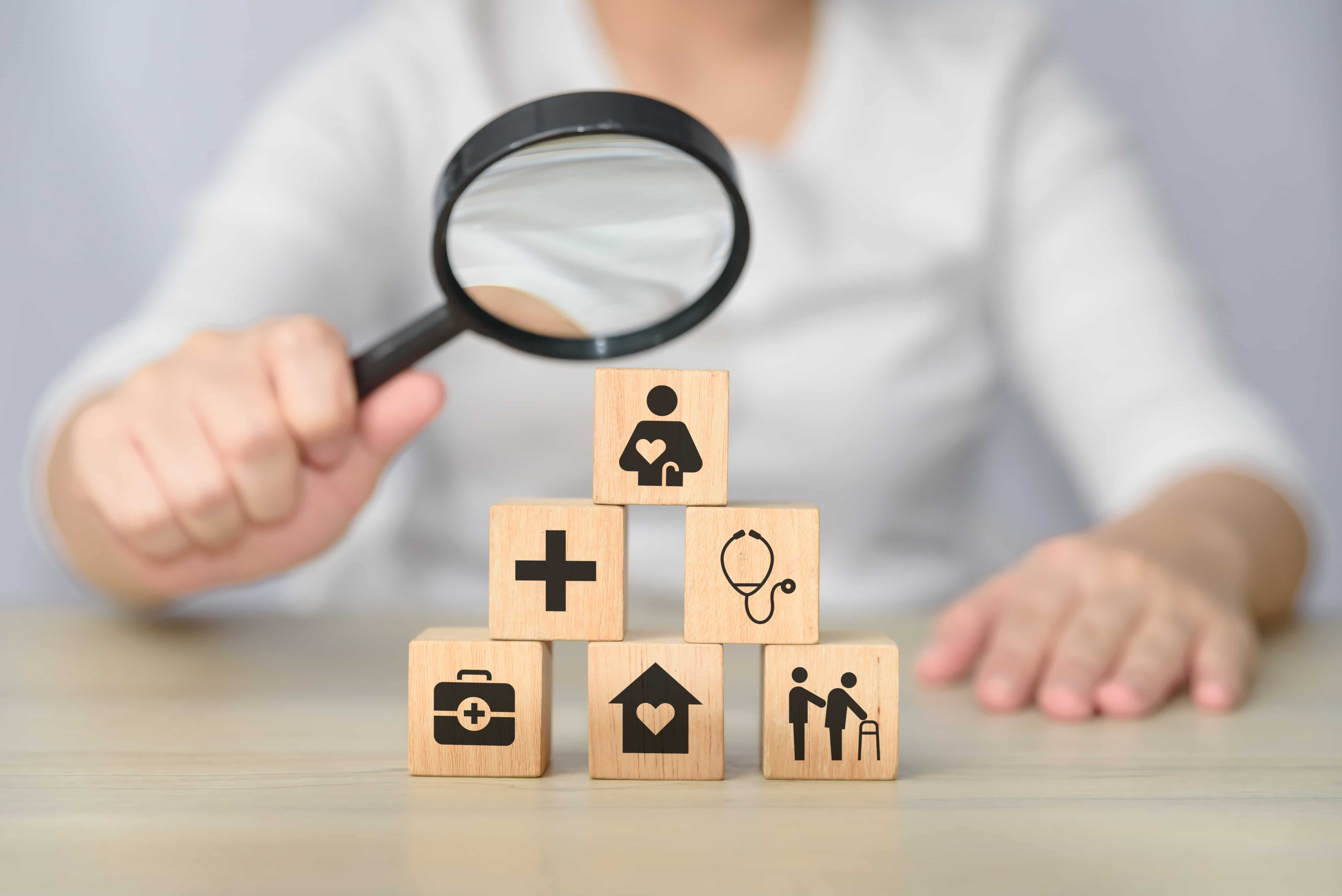 Woman holding a magnifying glass over wooden blocks with healthcare symbols