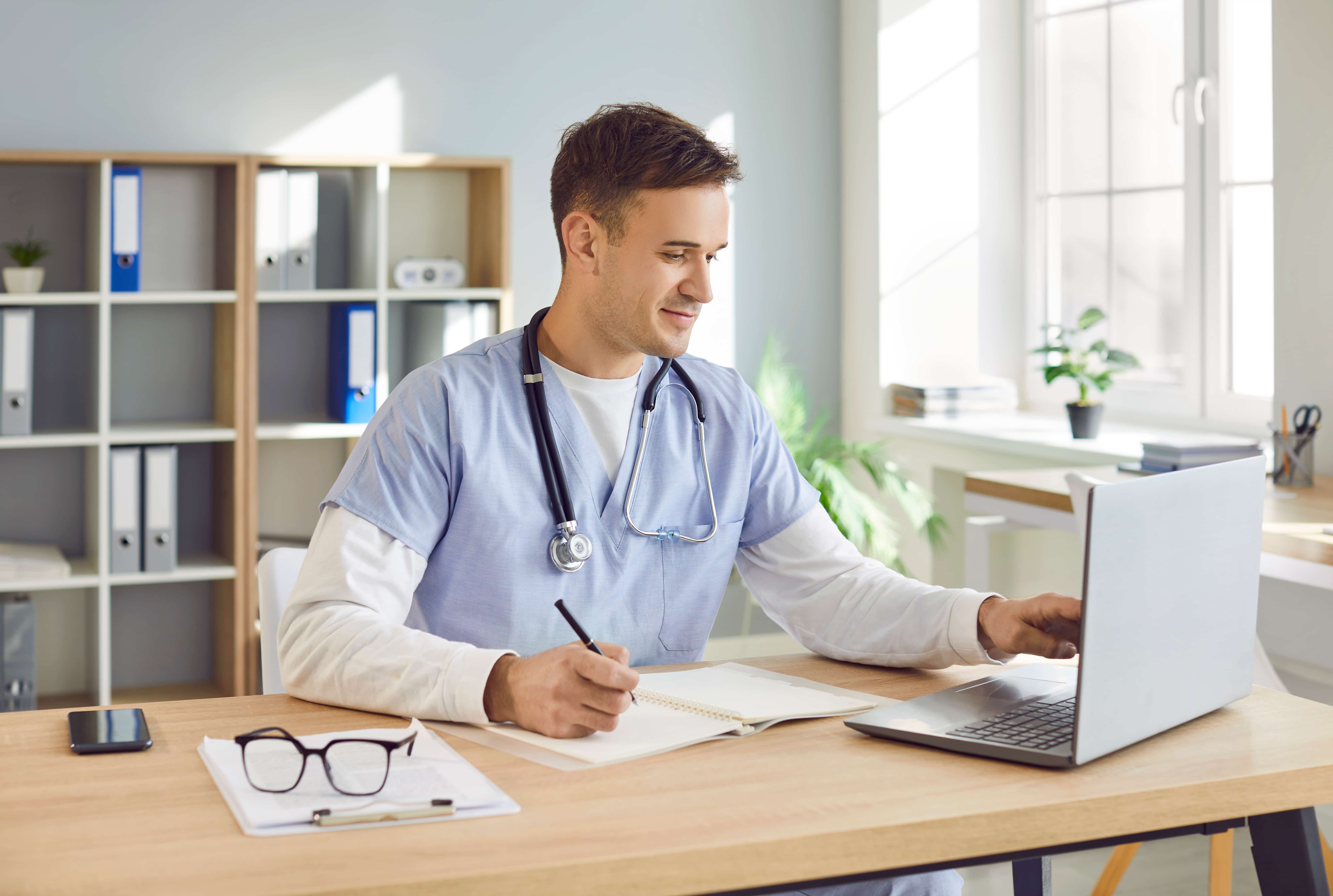 Male nurse typing on a laptop at a desk