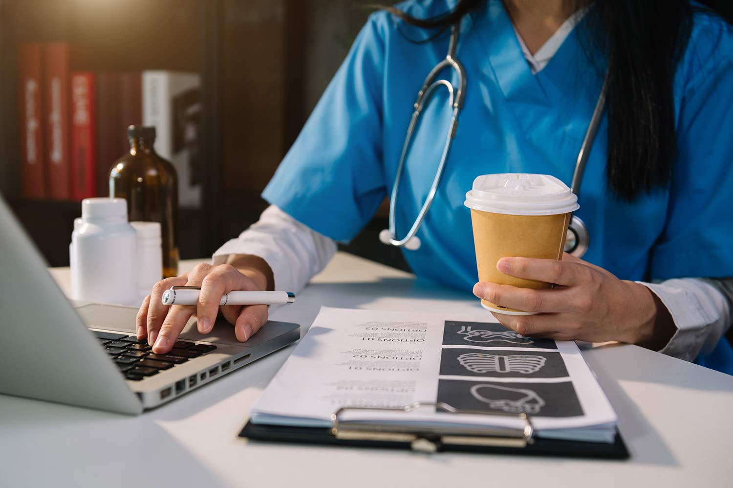 Close up of a nurse with coffee and using a laptop